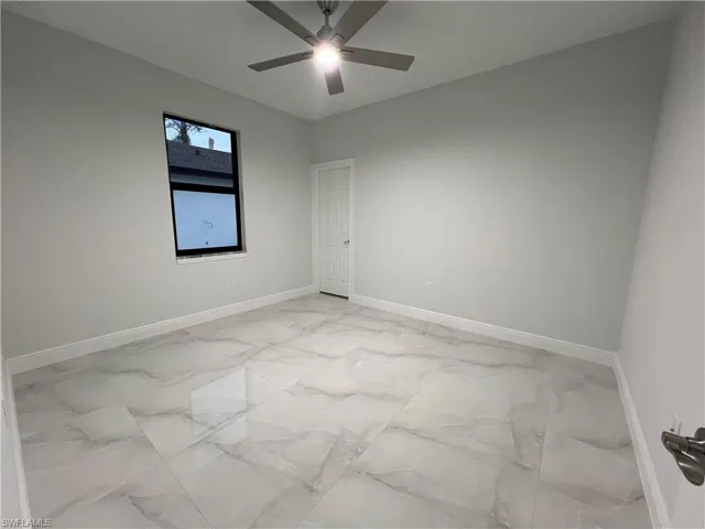 Empty room featuring a ceiling fan, marble finish floor, and baseboards