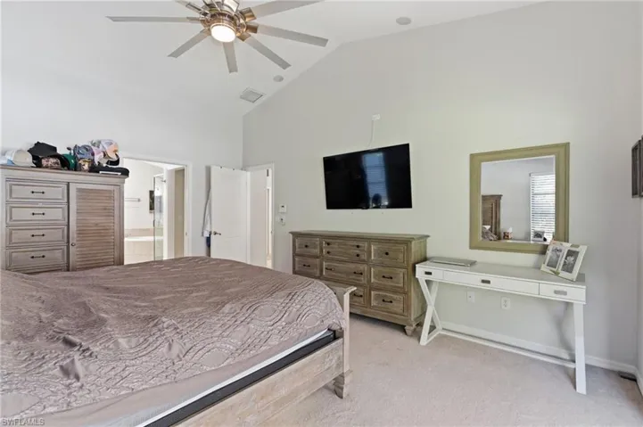 Bedroom with vaulted ceiling, light carpet, a ceiling fan, and ensuite bath