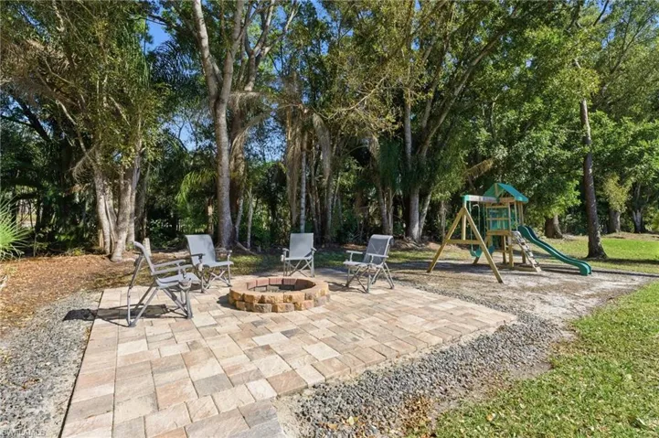 View of patio featuring a playground, an outdoor fire pit, and view of wooded area