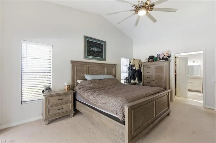 Bedroom featuring lofted ceiling, light colored carpet, a ceiling fan, and ensuite bath