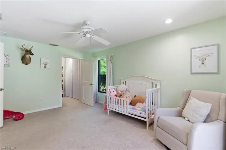 Bedroom featuring light colored carpet, a nursery area, and ceiling fan