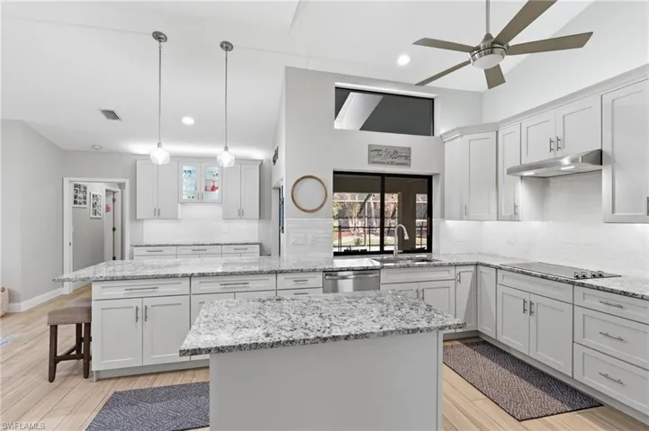 Kitchen featuring a kitchen island, light wood-style floors, white cabinets, and light stone countertops