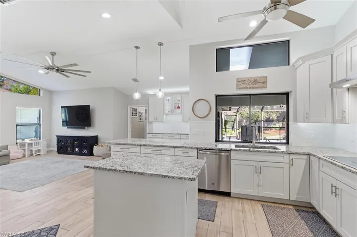 Kitchen featuring ceiling fan, white cabinets, light stone countertops, decorative backsplash, and vaulted ceiling