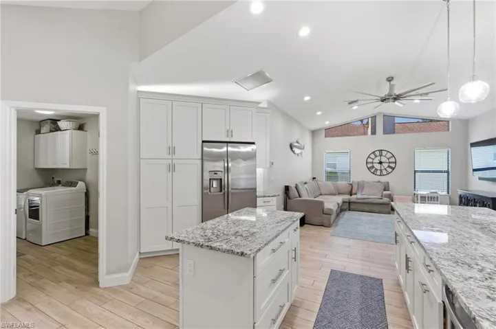 Kitchen with ceiling fan, white cabinetry, open floor plan, stainless steel fridge with ice dispenser, and light stone counters
