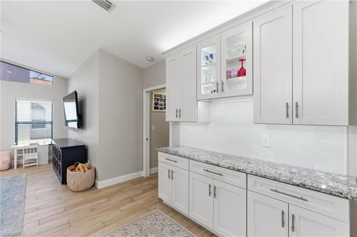 Kitchen featuring white cabinets, glass insert cabinets, light wood-style floors, light stone countertops, and lofted ceiling