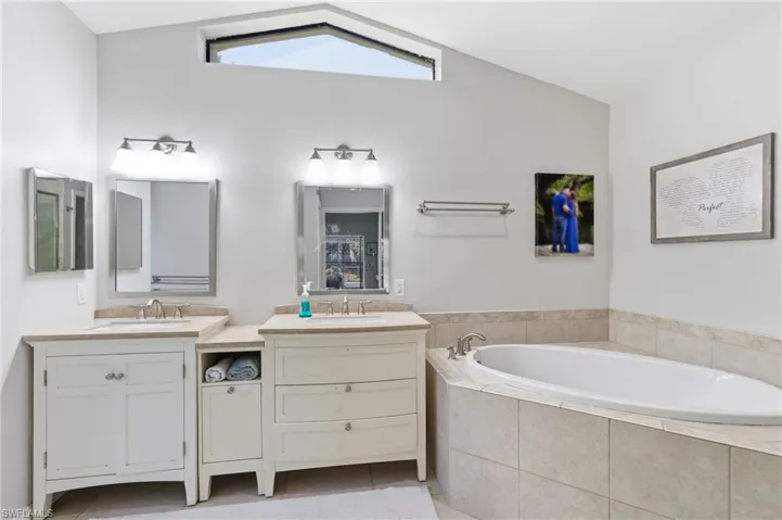 Bathroom featuring light tile patterned floors, two vanities, a bath, and vaulted ceiling