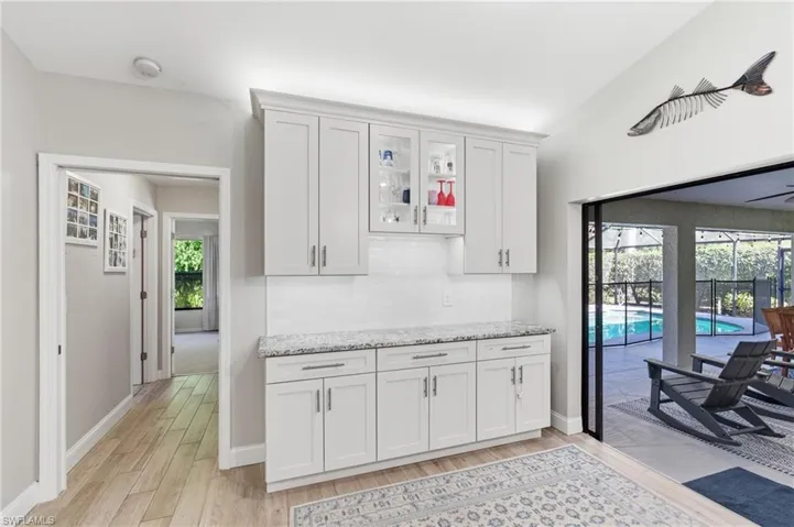 Kitchen featuring white cabinets, light wood-style floors, light stone countertops, and glass insert cabinets