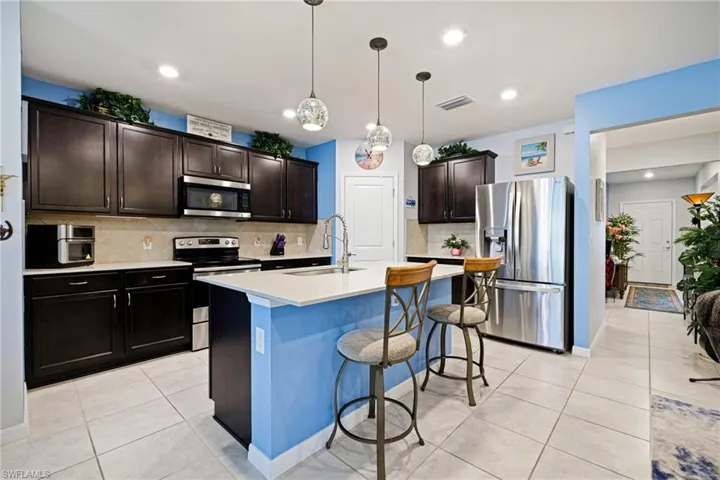 Kitchen featuring stainless steel appliances, dark wood finish cabinetry, light tile patterned flooring, a center island with sink, and hanging light fixtures