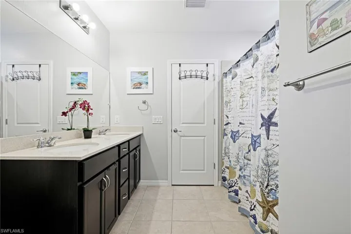Bathroom featuring double vanity, curtained shower, and light tile patterned floors