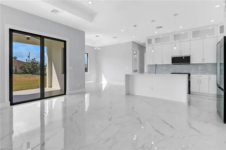 Kitchen with sink, white cabinets, backsplash, appliances with stainless steel finishes, and decorative light fixtures