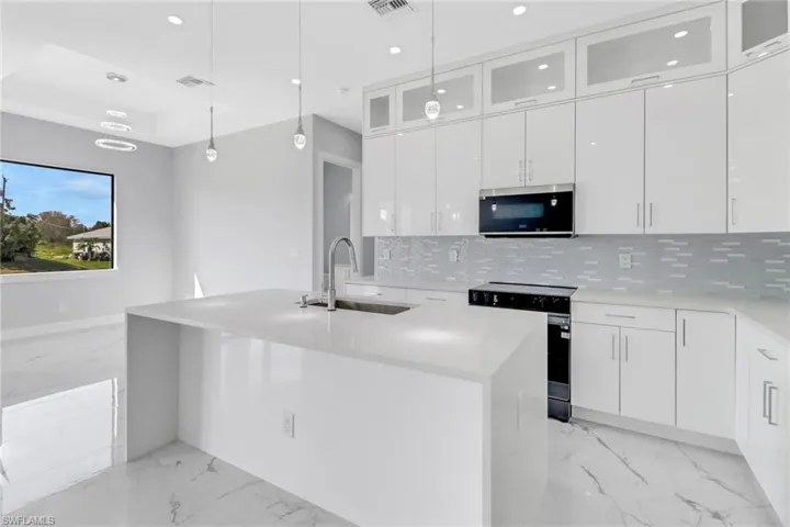 Kitchen featuring sink, white cabinetry, a center island with sink, appliances with stainless steel finishes, and decorative light fixtures