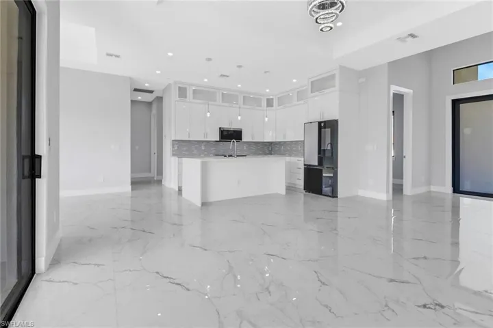 Kitchen featuring black fridge, sink, an island with sink, white cabinetry, and hanging light fixtures