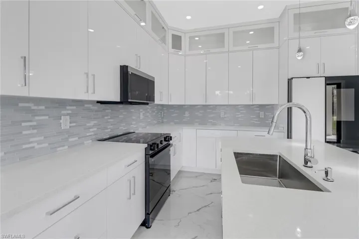 Kitchen with backsplash, sink, black range with electric stovetop, and white cabinets