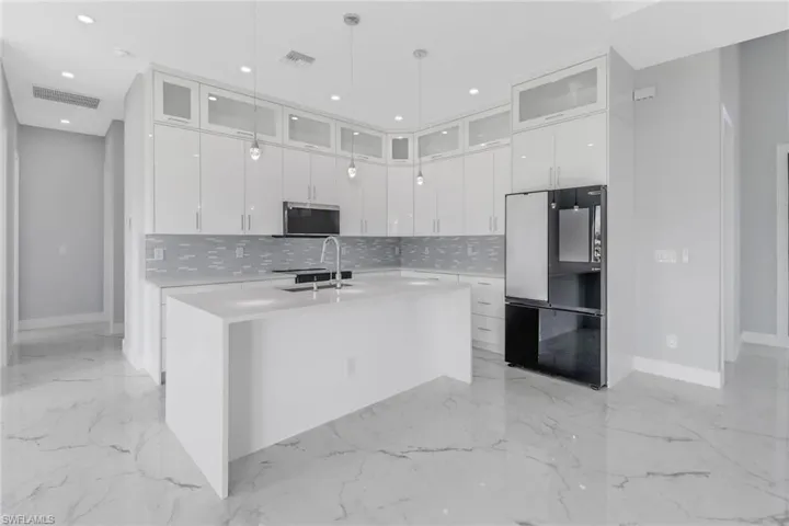 Kitchen featuring white cabinets, sink, a kitchen island with sink, and black refrigerator