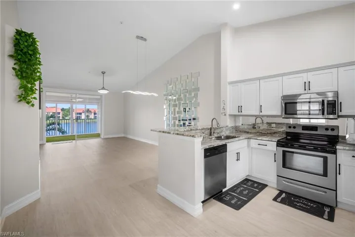 Kitchen featuring stainless steel appliances, high vaulted ceiling, light stone counters, white cabinets, and light wood-style flooring