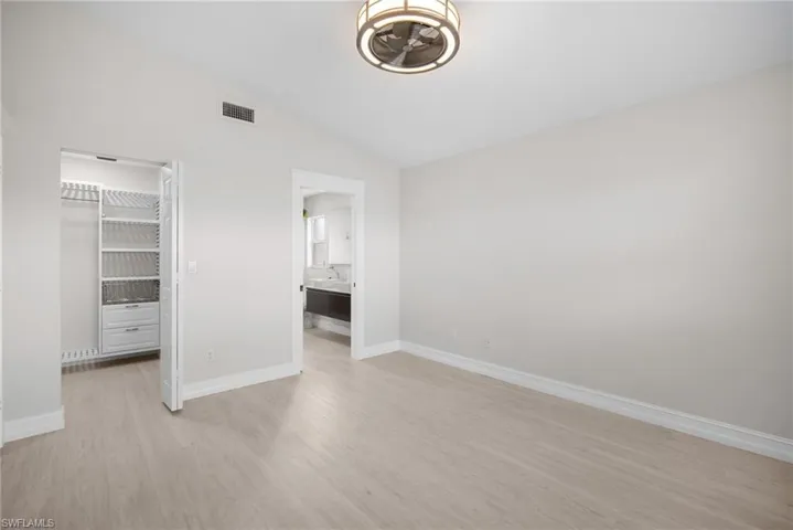 Unfurnished bedroom featuring a walk in closet, lofted ceiling, and light wood finished floors