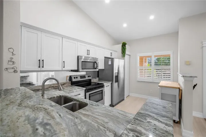 Kitchen featuring stainless steel appliances, light stone counters, light wood finished floors, lofted ceiling, and recessed lighting