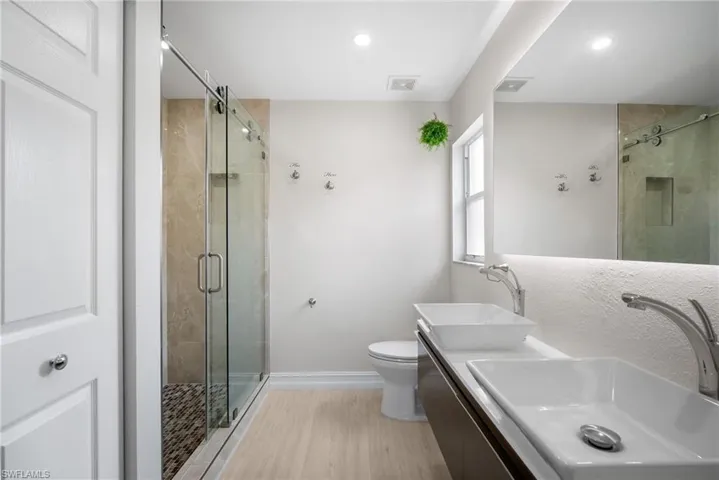 Full bathroom featuring double vanity, a shower stall, light wood-type flooring, and recessed lighting