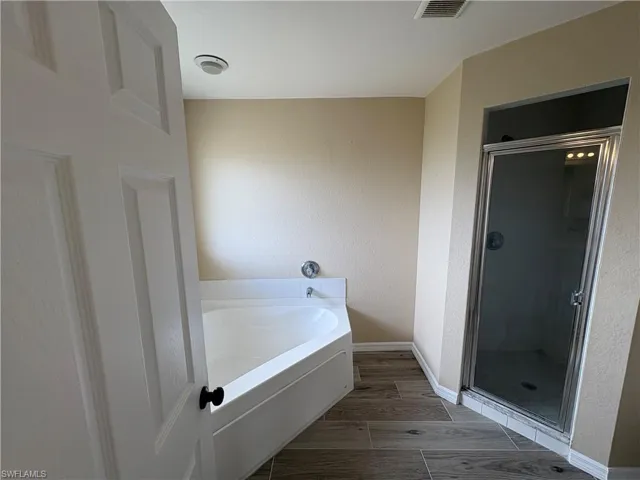Full bathroom with wood tiled floors, a shower stall, a garden tub, and a textured wall
