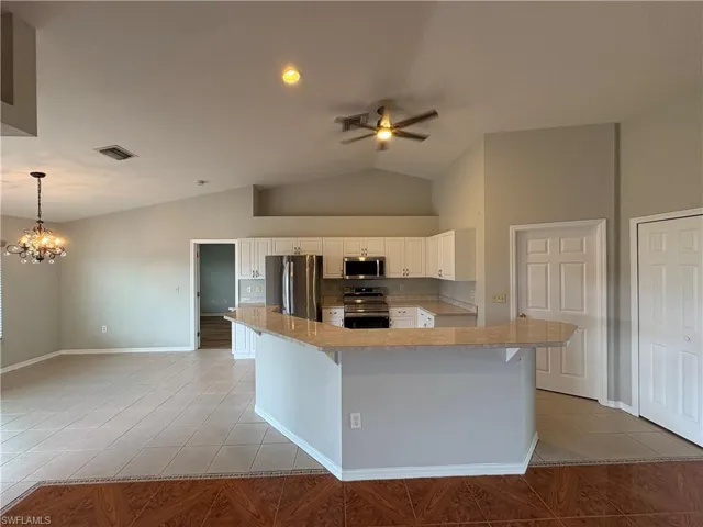 Kitchen with light tile patterned flooring, stainless steel appliances, white cabinetry, vaulted ceiling, and a kitchen island