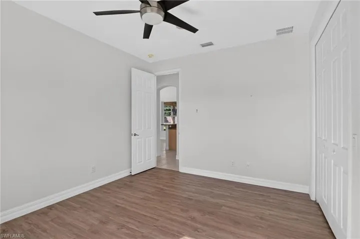 Wood-finish flooring with white baseboards, a ceiling fan, and white paneled doors