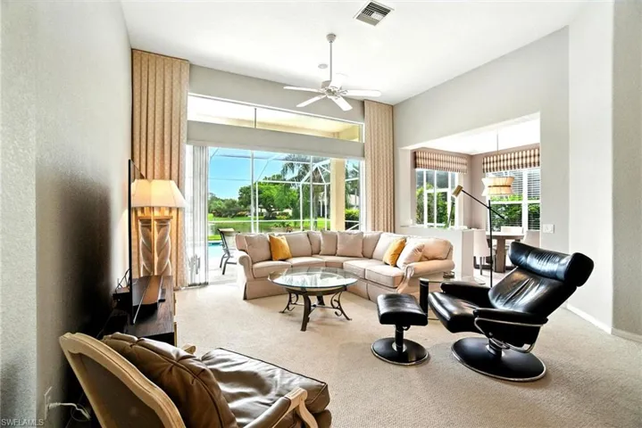 Carpeted living area featuring a sunroom, ceiling fan, and a textured wall