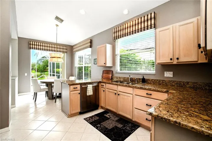 Kitchen featuring light brown cabinetry, dark stone countertops, a peninsula, dishwashing machine, and recessed lighting