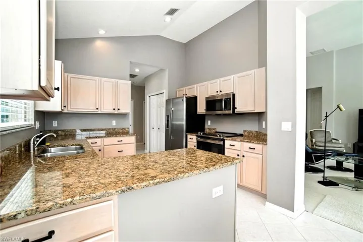 Kitchen featuring dark stone countertops, light brown cabinetry, stainless steel appliances, a peninsula, and high vaulted ceiling
