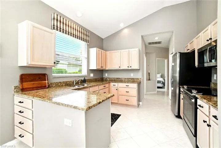 Kitchen with electric range, dark stone countertops, stainless steel microwave, vaulted ceiling, and a peninsula