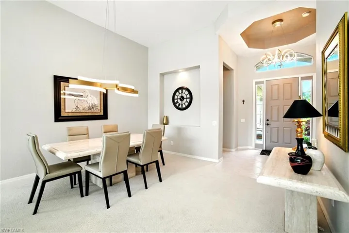 Dining area with a chandelier, a raised ceiling, light colored carpet, a towering ceiling, and light tile patterned floors