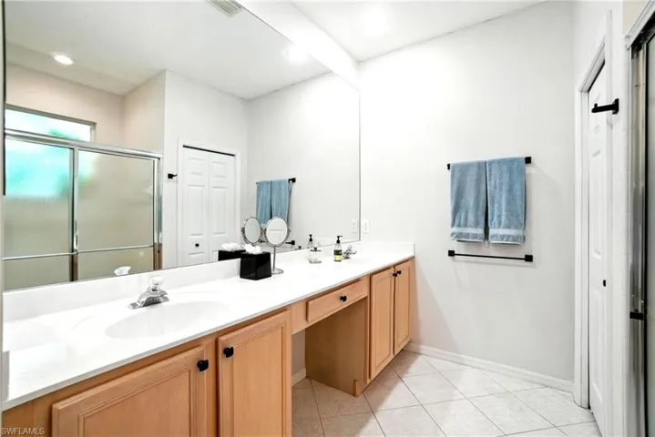 Bathroom with double vanity, a shower stall, a closet, light tile patterned floors, and recessed lighting