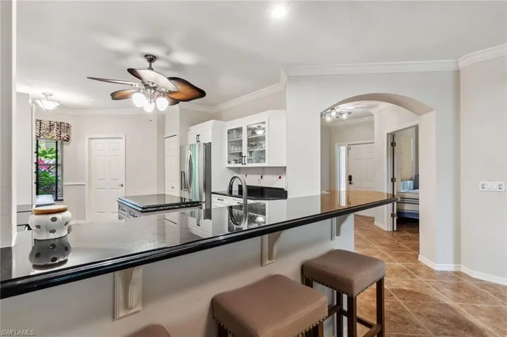 Kitchen featuring dark countertops, stainless steel fridge with ice dispenser, a breakfast bar area, arched walkways, and a ceiling fan
