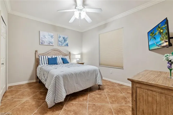 Bedroom with light tile patterned floors, baseboards, ornamental molding, and a ceiling fan