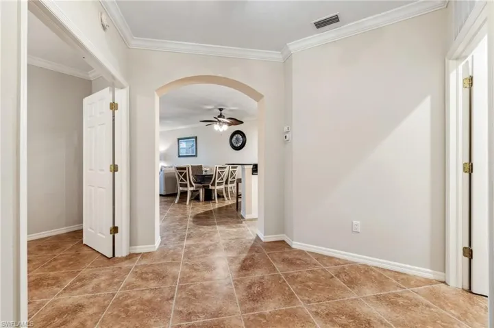 Hallway with crown molding, arched walkways, baseboards, and visible vents