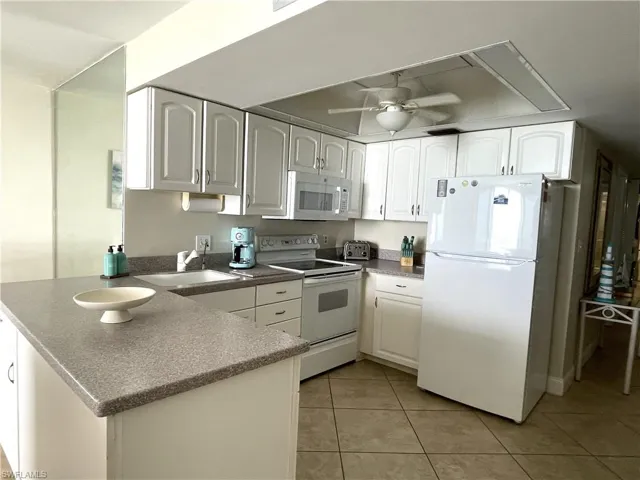 Kitchen featuring white appliances, a ceiling fan, white cabinetry, a peninsula, and tile floors