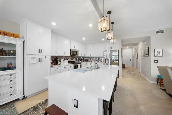 Kitchen featuring a kitchen island with sink, a kitchen breakfast bar, white cabinetry, backsplash, and stainless steel appliances