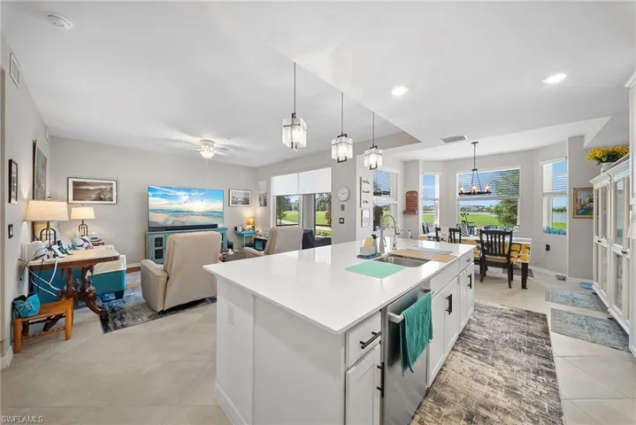 Kitchen featuring white cabinets, a kitchen island with sink, open floor plan, stainless steel dishwasher, and suspended lighting