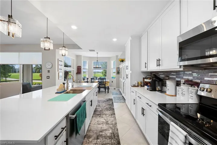 Kitchen with stainless steel appliances, a large island with sink, white cabinets, and light stone counters