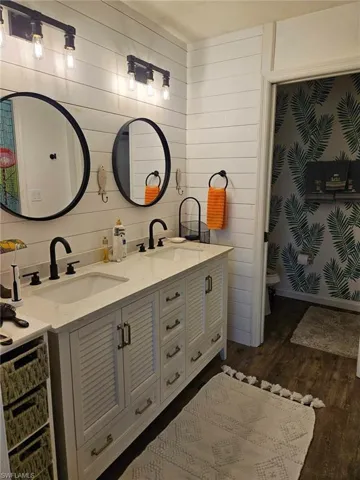 Full bath featuring double vanity, dark wood-type flooring, and wooden walls