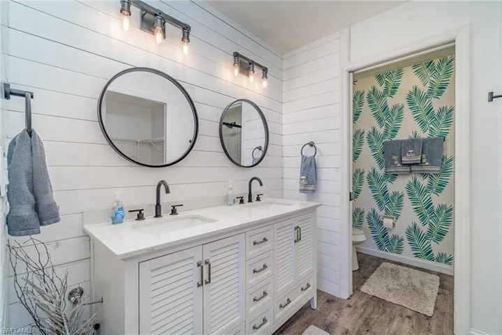 Full bathroom featuring double vanity, dark wood-type flooring, and wooden walls