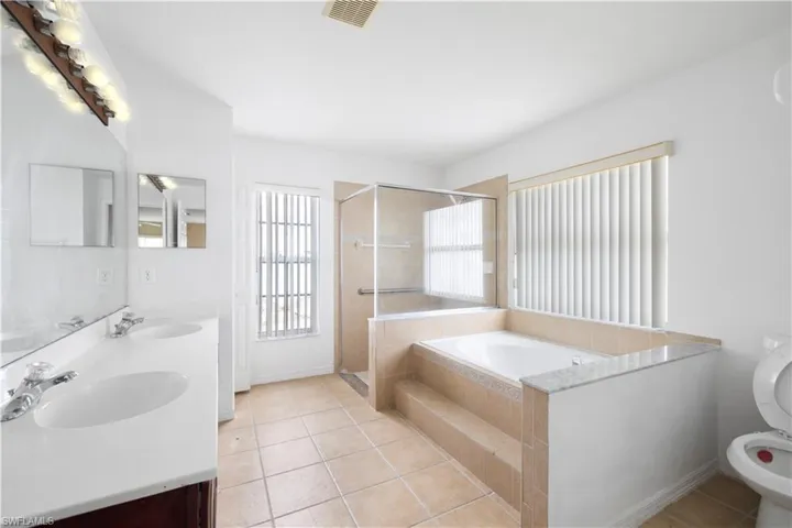 Full bathroom featuring double vanity, shower with separate bathtub, toilet, and tile floors