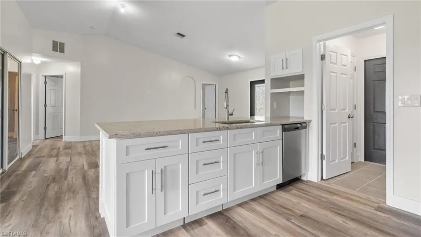 Kitchen featuring white cabinetry, lofted ceiling, stainless steel dishwasher, and sink