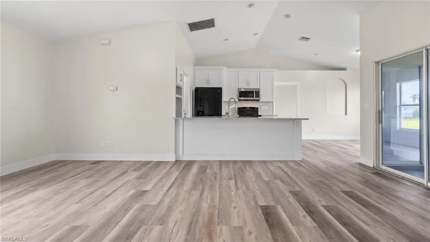 Kitchen featuring black fridge, light stone counters, vaulted ceiling, white cabinets, and light hardwood / wood-style flooring