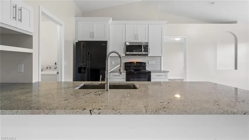 Kitchen with white cabinetry, black appliances, lofted ceiling, and light stone countertops