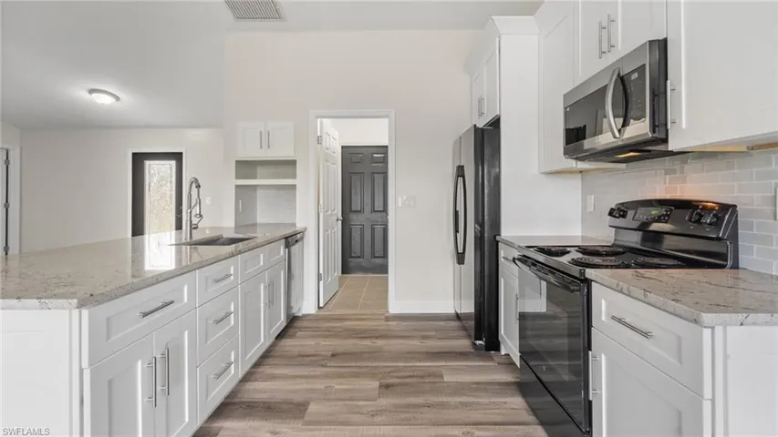 Kitchen featuring stainless steel appliances, white cabinetry, sink, light stone countertops, and light wood-type flooring