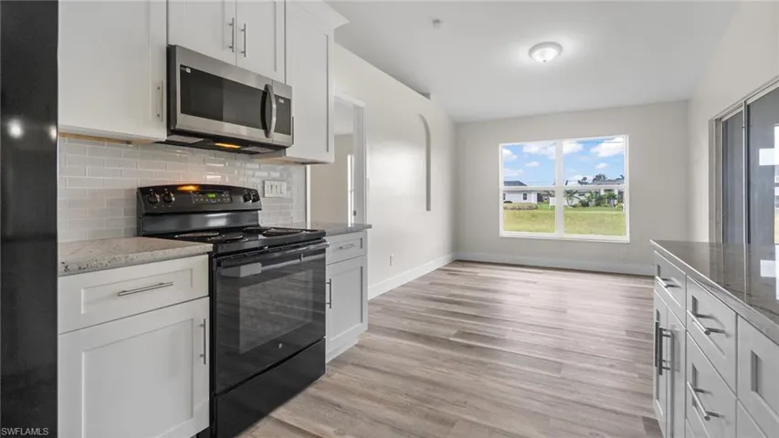 Kitchen with black appliances, white cabinetry, light wood-type flooring, and light stone countertops