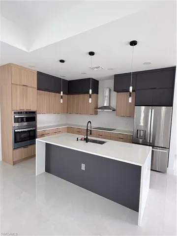 Kitchen featuring modern cabinets, light stone countertops, fridge, exhaust hood, and two tone cabinets