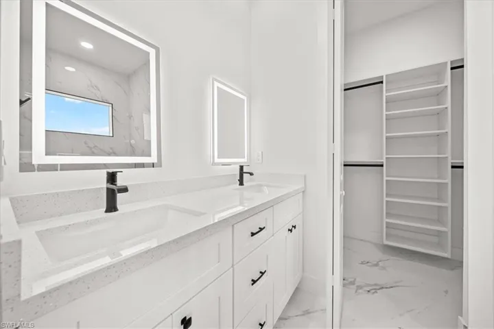Full bath featuring marble look tiles, double vanity, a walk in closet, and recessed lighting
