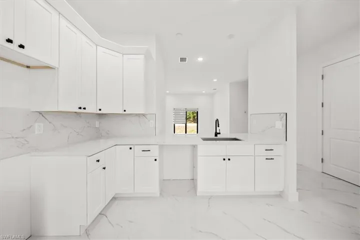 Kitchen with light marble finish flooring, recessed lighting, backsplash, white cabinetry, and a peninsula