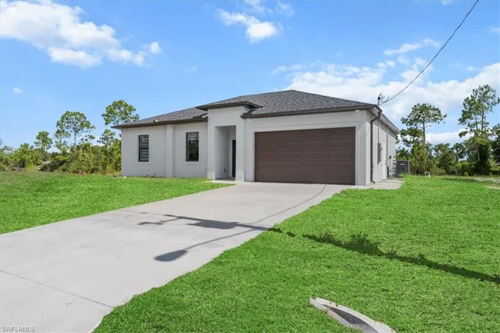 Prairie-style home with stucco siding, driveway, an attached garage, and a front lawn